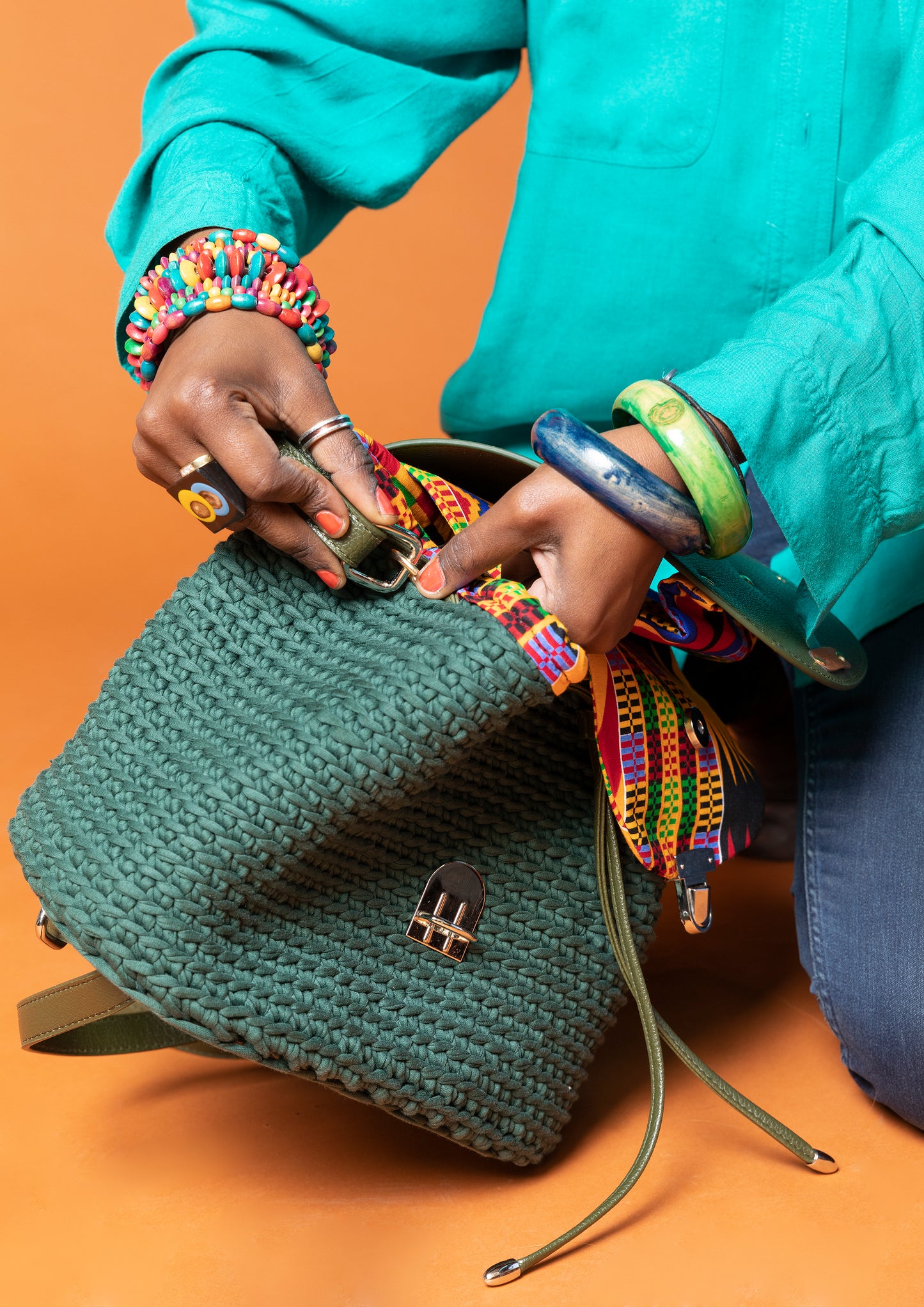crocheted, forest/ oak green bag, with an African style print. Model shown adjusting straps.